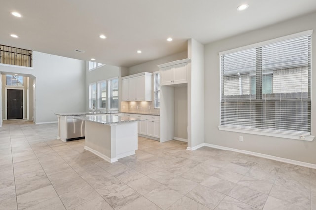 kitchen featuring a center island, backsplash, white cabinets, light stone countertops, and baseboards