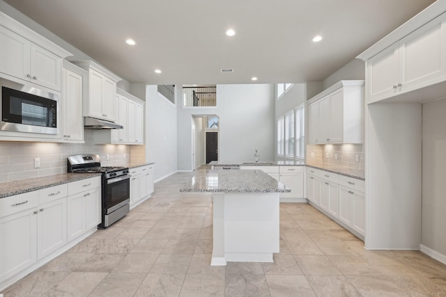 kitchen with a kitchen island, light stone countertops, stainless steel gas range, built in microwave, and under cabinet range hood