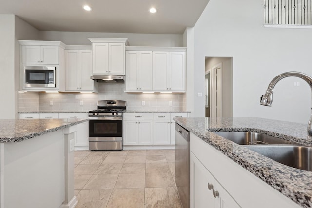 kitchen featuring appliances with stainless steel finishes, white cabinets, a sink, light stone countertops, and under cabinet range hood