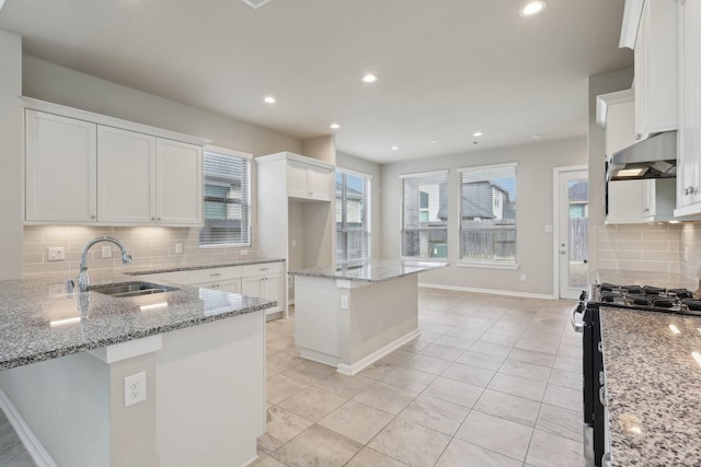 kitchen with light stone counters, white cabinetry, a sink, black stove, and under cabinet range hood