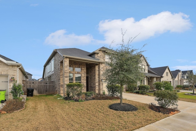 view of front facade with brick siding, concrete driveway, a residential view, fence, and a front yard