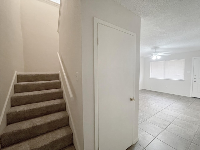 staircase featuring a textured ceiling, a ceiling fan, and tile patterned floors