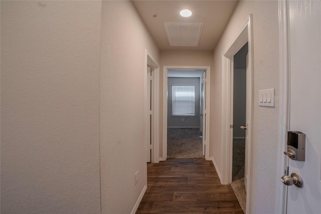 hallway with dark wood-style floors, a textured wall, and baseboards