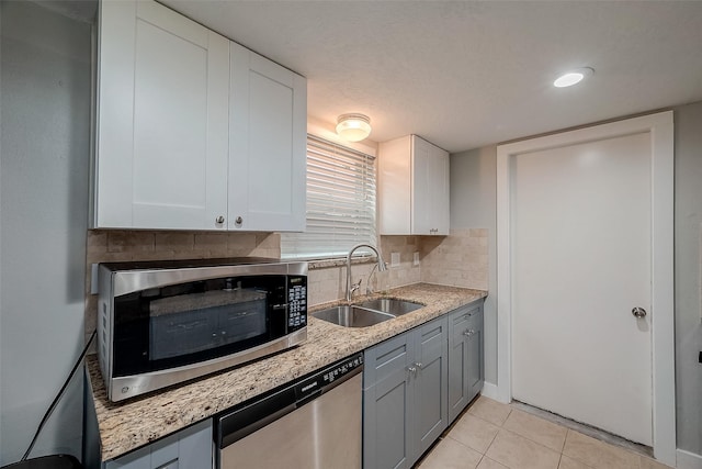 kitchen featuring light tile patterned floors, stainless steel appliances, backsplash, white cabinetry, and a sink