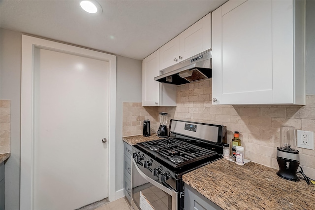 kitchen featuring light stone countertops, under cabinet range hood, white cabinetry, backsplash, and gas stove