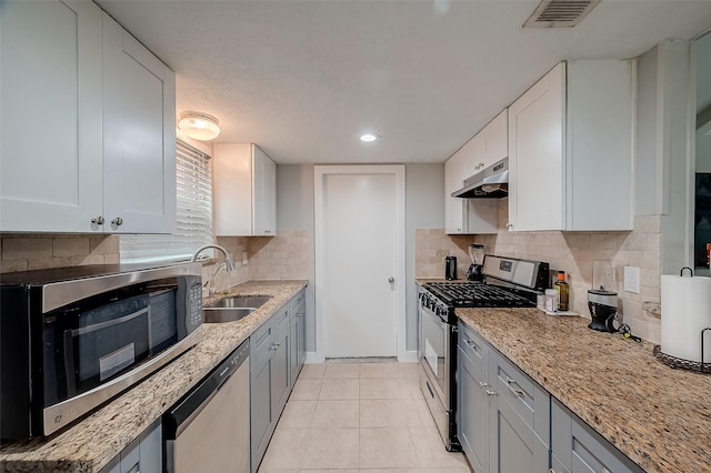 kitchen featuring under cabinet range hood, a sink, white cabinetry, appliances with stainless steel finishes, and tasteful backsplash