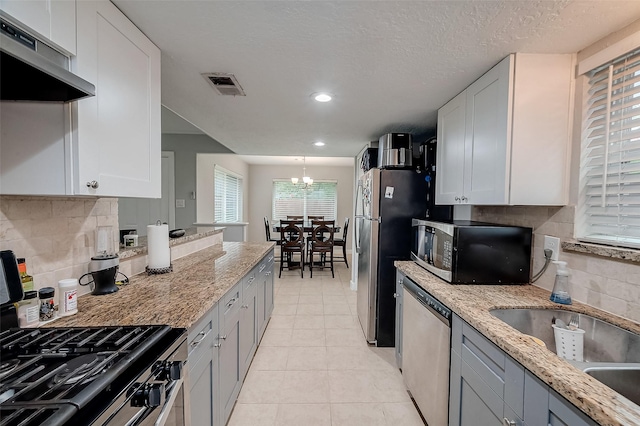 kitchen with visible vents, appliances with stainless steel finishes, light stone counters, under cabinet range hood, and white cabinetry