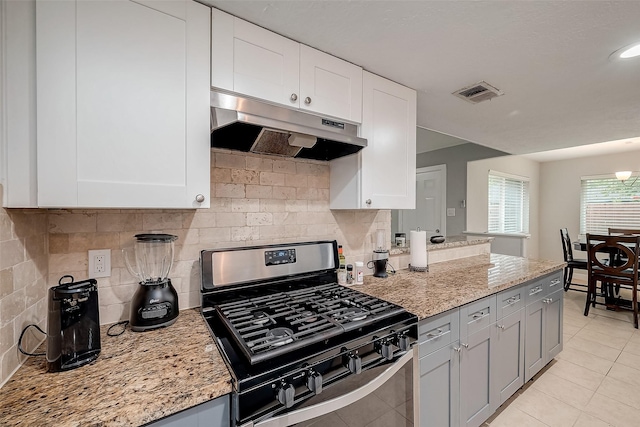 kitchen with light stone countertops, under cabinet range hood, visible vents, and range with gas stovetop