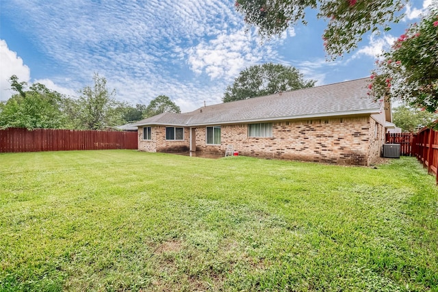 rear view of house featuring brick siding, a lawn, central AC unit, and a fenced backyard