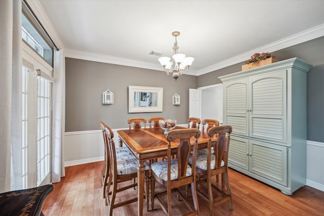 dining area with ornamental molding, light wood finished floors, visible vents, and a notable chandelier