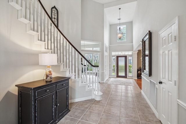 foyer with light tile patterned flooring, a high ceiling, visible vents, baseboards, and stairs