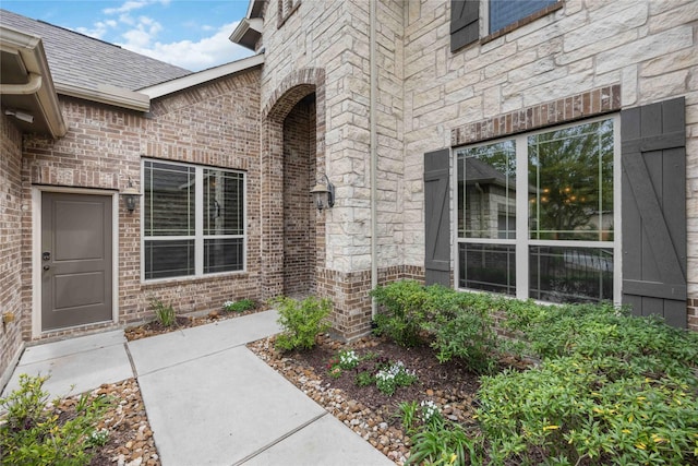 property entrance with a shingled roof and brick siding