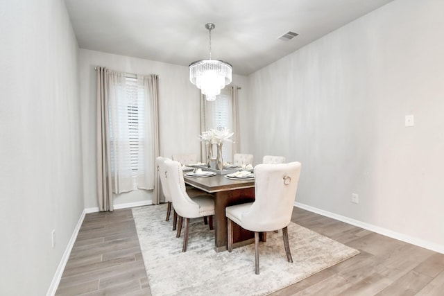 dining space with baseboards, wood finished floors, visible vents, and a notable chandelier