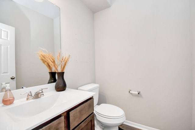 half bath featuring vanity, toilet, and baseboards