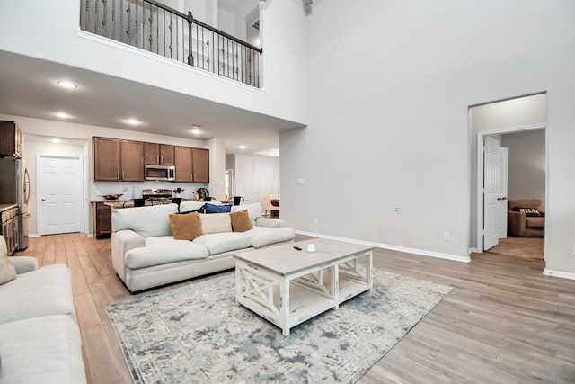 living room with light wood-style floors, a high ceiling, baseboards, and recessed lighting