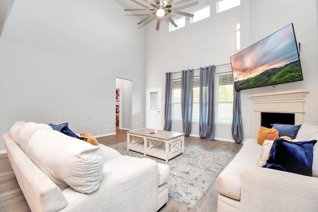 living area with baseboards, a towering ceiling, light wood-style flooring, ceiling fan, and a fireplace