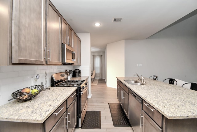 kitchen with visible vents, light stone counters, a kitchen island with sink, stainless steel appliances, and a sink