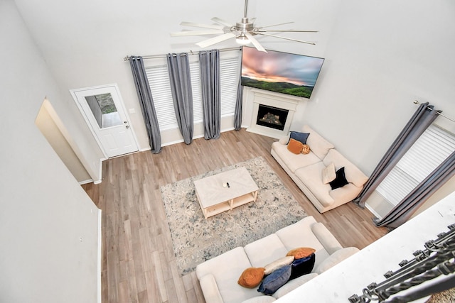 living area with light wood finished floors, a fireplace, baseboards, and a ceiling fan