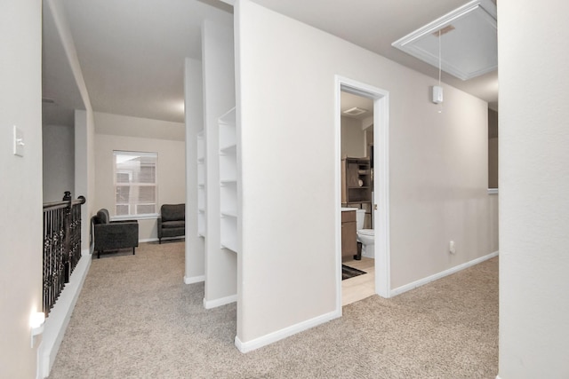 hallway with attic access, light colored carpet, and baseboards