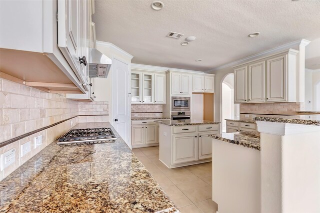 13006 Freemont Peak Ln, Humble, TX 77346 - kitchen featuring stainless steel appliances, decorative backsplash, arched walkways, light stone counters, and a textured ceiling
