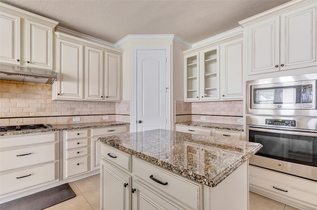 13006 Freemont Peak Ln, Humble, TX 77346 - kitchen featuring appliances with stainless steel finishes, under cabinet range hood, stone counters, tasteful backsplash, and glass insert cabinets