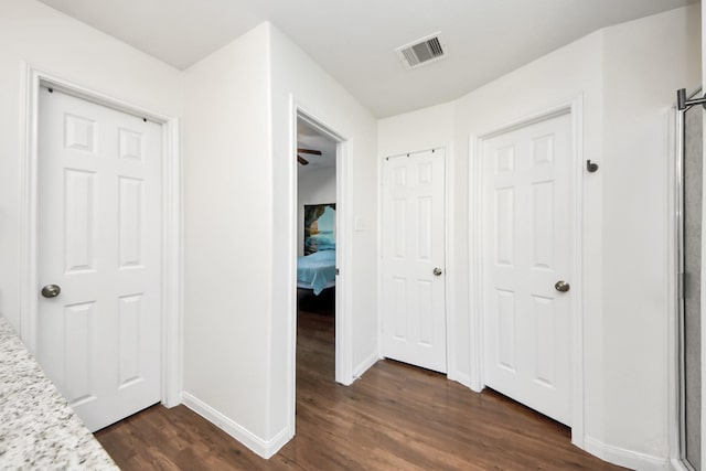 corridor with dark wood-style floors, visible vents, and baseboards