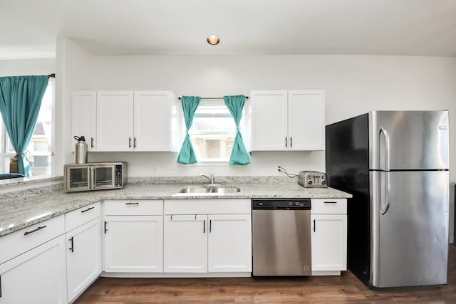 kitchen with appliances with stainless steel finishes, a sink, light stone counters, and white cabinets