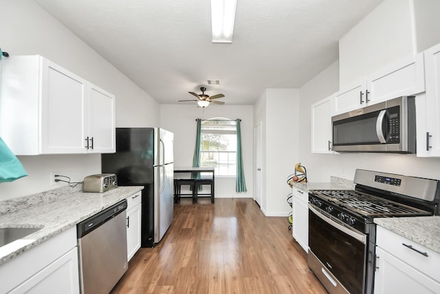 kitchen with visible vents, light stone counters, appliances with stainless steel finishes, and white cabinetry