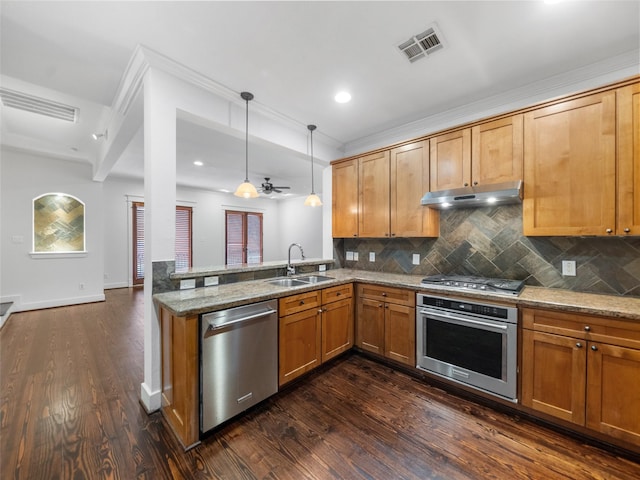 kitchen featuring light stone counters, hanging light fixtures, appliances with stainless steel finishes, a sink, and under cabinet range hood