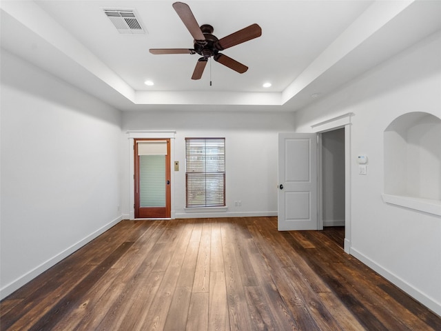 empty room featuring dark wood-type flooring, a raised ceiling, visible vents, and baseboards