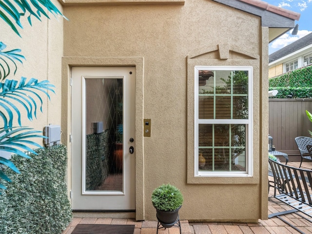 view of exterior entry featuring fence and stucco siding