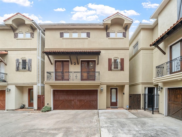 multi unit property featuring a garage, a balcony, driveway, and stucco siding