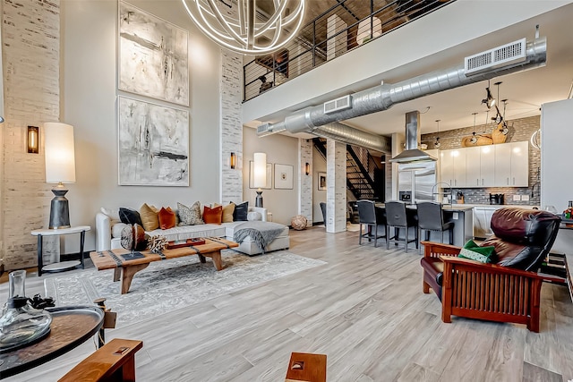 living room featuring light wood-style floors, visible vents, a towering ceiling, and stairs