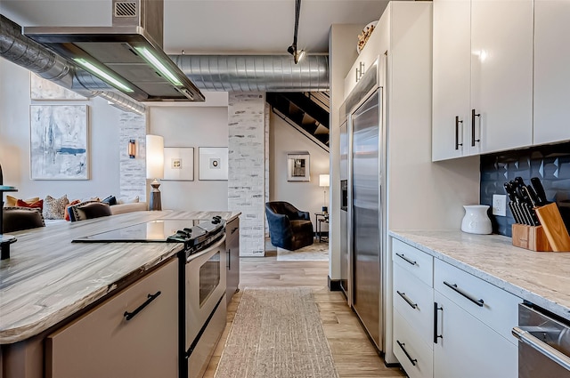 505 Bastrop St Unit 508, Houston, TX 77003 - kitchen with appliances with stainless steel finishes, light wood-type flooring, white cabinetry, and exhaust hood