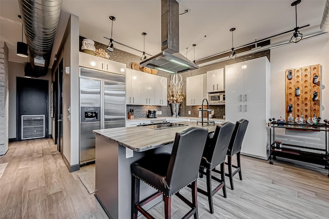 kitchen with a center island, pendant lighting, island exhaust hood, white cabinets, and built in appliances