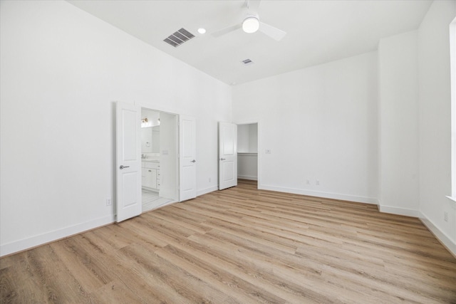 unfurnished bedroom with light wood finished floors, baseboards, visible vents, connected bathroom, and a high ceiling