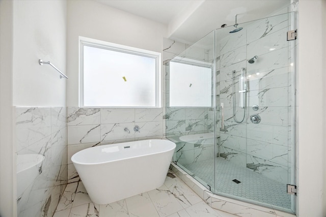 bathroom featuring marble finish floor, a freestanding tub, a marble finish shower, and tile walls