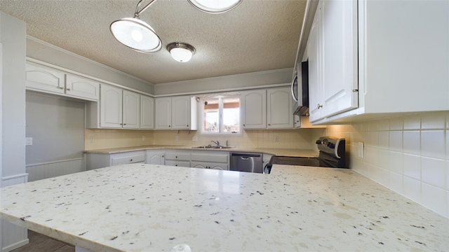 kitchen featuring white cabinets, appliances with stainless steel finishes, a peninsula, crown molding, and a sink