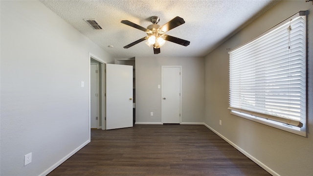 unfurnished bedroom featuring baseboards, visible vents, a ceiling fan, dark wood-style flooring, and a textured ceiling