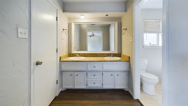 bathroom featuring toilet, double vanity, baseboards, and a sink