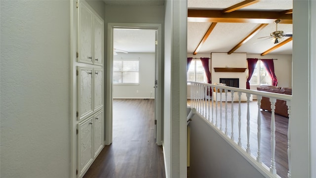 corridor featuring a textured wall, a textured ceiling, beamed ceiling, and wood finished floors