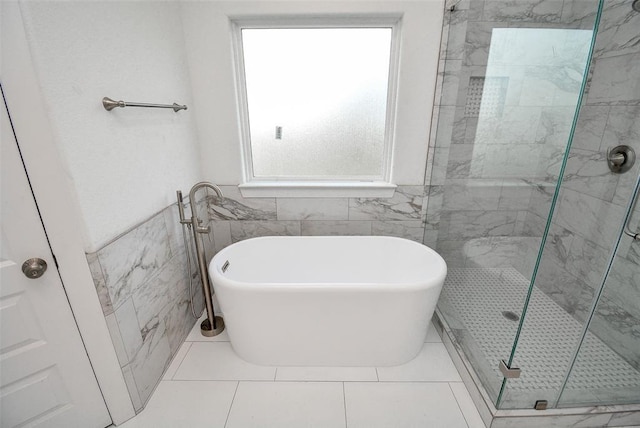 bathroom featuring a soaking tub, wainscoting, tile walls, and a stall shower