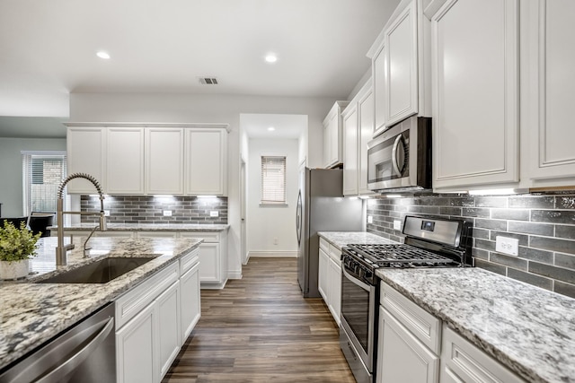 kitchen featuring decorative backsplash, dark wood-style floors, stainless steel appliances, white cabinetry, and a sink