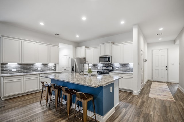 kitchen with an island with sink, dark wood-style floors, appliances with stainless steel finishes, a breakfast bar, and white cabinetry