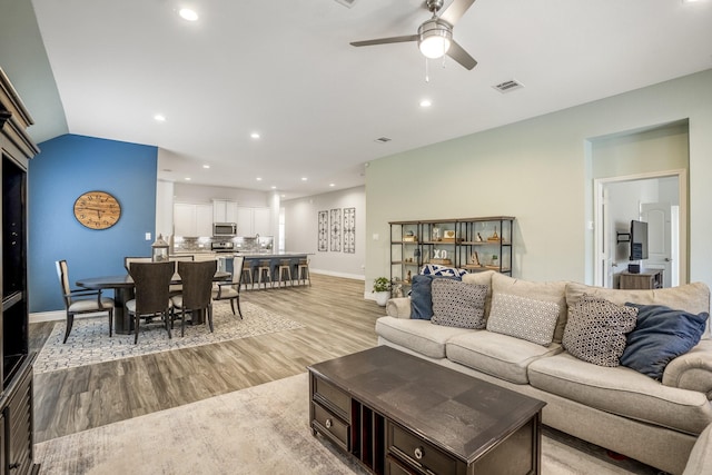 living room featuring light wood finished floors, recessed lighting, lofted ceiling, visible vents, and baseboards