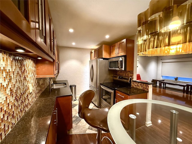 kitchen featuring a sink, appliances with stainless steel finishes, backsplash, brown cabinetry, and dark wood finished floors