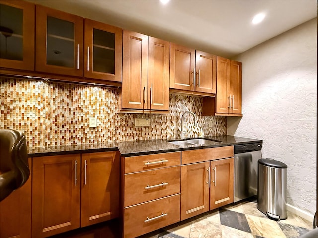 kitchen featuring glass insert cabinets, backsplash, brown cabinets, stainless steel dishwasher, and a sink