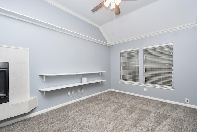 carpeted empty room featuring a tile fireplace, a ceiling fan, baseboards, vaulted ceiling, and ornamental molding