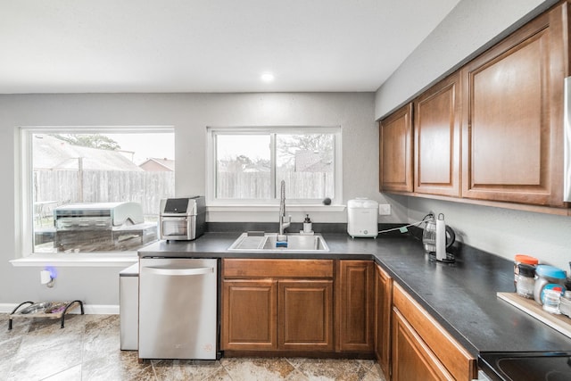 kitchen with brown cabinetry, dark countertops, a sink, and dishwasher