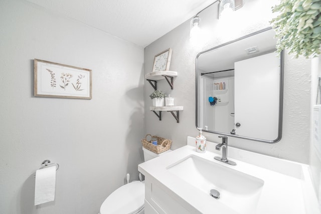 bathroom featuring visible vents, a textured wall, vanity, and toilet